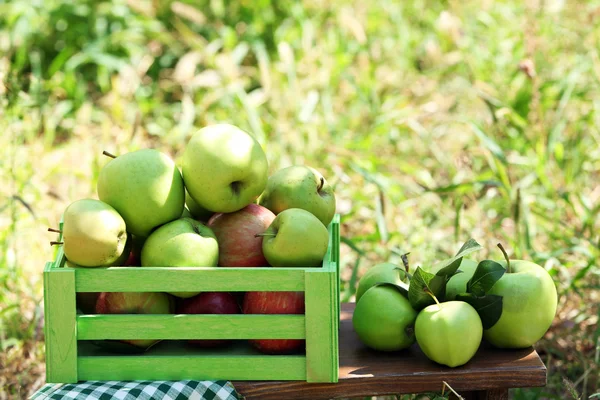Šťavnatá jablka v dřevěné krabici na trávě, venku — Stock fotografie
