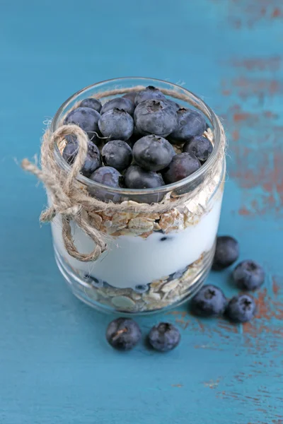 Hälsosam frukost - yoghurt med blåbär och müsli serveras i glasburk, på färg trä bakgrund — Stockfoto