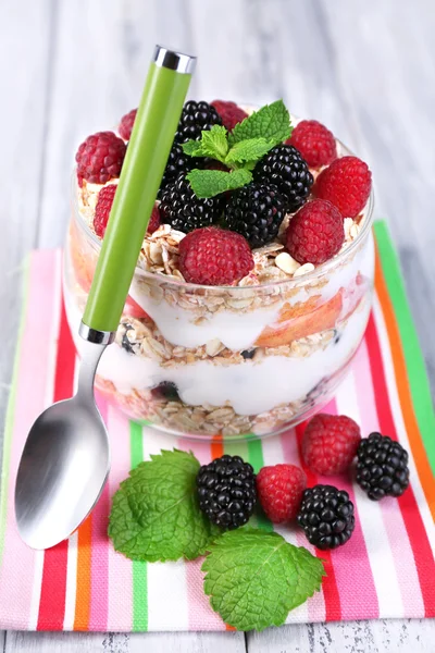 Gezond ontbijt - yoghurt met vers fruit, bessen en muesli geserveerd in glazen pot, op een houten achtergrond kleur — Stockfoto