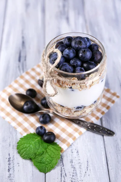 V sklenice, na barevné dřevěné pozadí podává Zdravá snídaně - jogurt s borůvkami a müsli — Stock fotografie