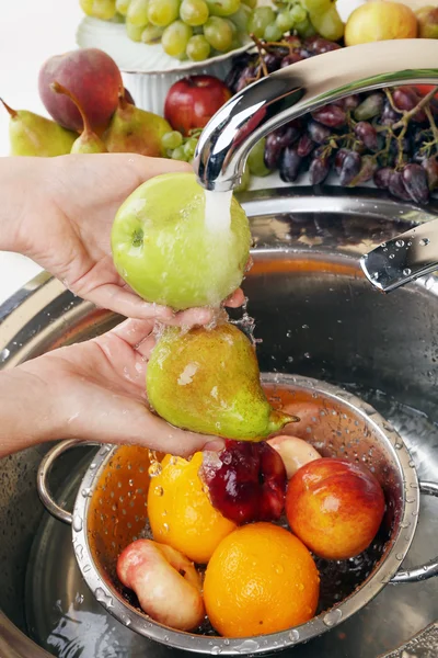 Женские руки мыть яблоко и другие фрукты в дуршлаге в раковине — стоковое фото
