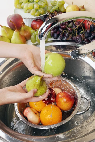 Женские руки мыть яблоко и другие фрукты в дуршлаге в раковине — стоковое фото