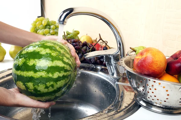 Las manos de la mujer lavando la sandía y otras frutas en el colador en el fregadero — Foto de Stock