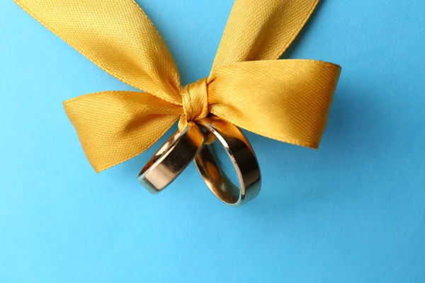 Wedding rings tied with ribbon on color background — Stock Photo, Image