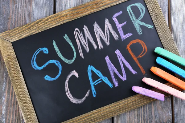 Text Summer camp written with chalk on chalkboard, and some chalk sticks of different colors — Stock Photo, Image