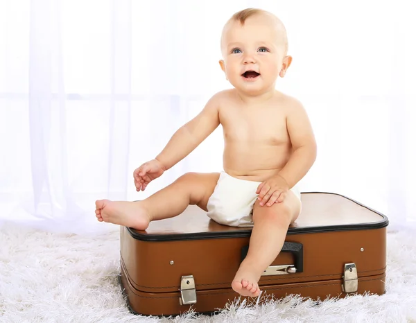 Lindo bebé niño sentado en la maleta en la habitación — Foto de Stock