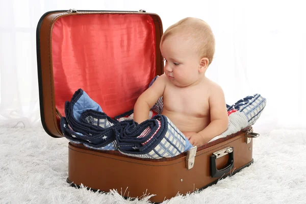 Lindo bebé niño sentado en la maleta en la habitación — Foto de Stock