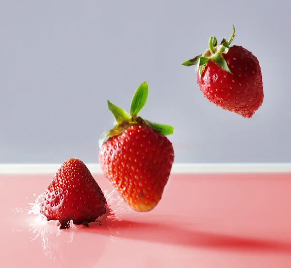 Delicious fresh strawberry falling into splashing milk — Stock Photo, Image