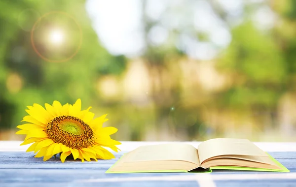 Aufgeschlagenes Buch mit Sonnenblume auf Tisch im Freien — Stockfoto
