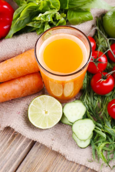 Szklanka świeżego soku z marchwi i warzywa na zwolnieniu serwetka na drewnianym stole — Zdjęcie stockowe