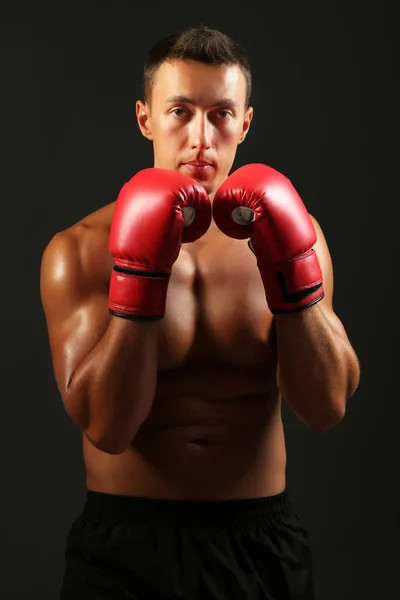 Bello giovane sportivo muscoloso con guanti da boxe su sfondo scuro — Foto Stock