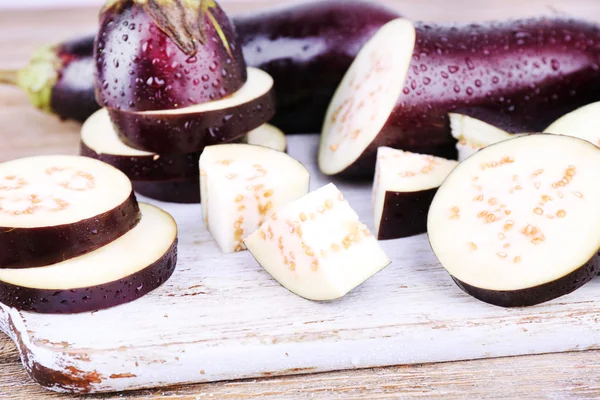 Chopped aubergines on cutting board on wooden background — Stock Photo, Image