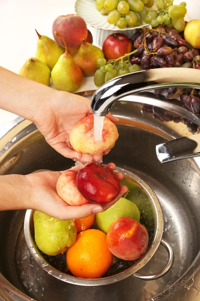 Руки женщины моют персики и другие фрукты в дуршлаге в раковине — стоковое фото