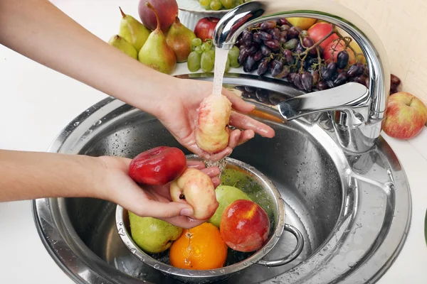 Wanita mencuci tangan persik dan buah-buahan lainnya di colander di wastafel — Stok Foto