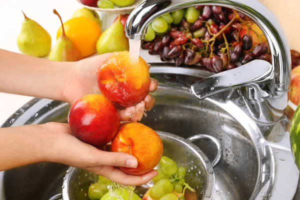 Woman's hands washing peaches and other fruits in colander in sink