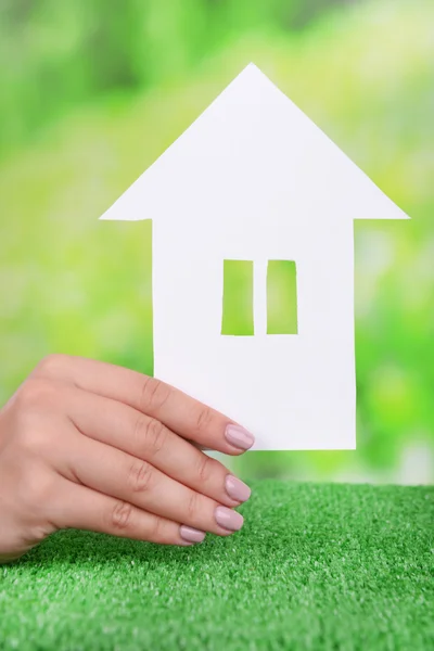 Mujer mano sosteniendo casa de papel sobre hierba sobre fondo brillante — Foto de Stock