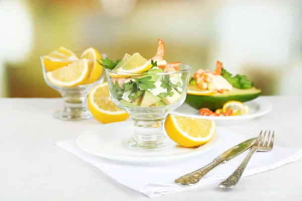 Tasty salads with shrimps and avocado in glass bowl and on plate, on table, on bright background — Stock Photo, Image