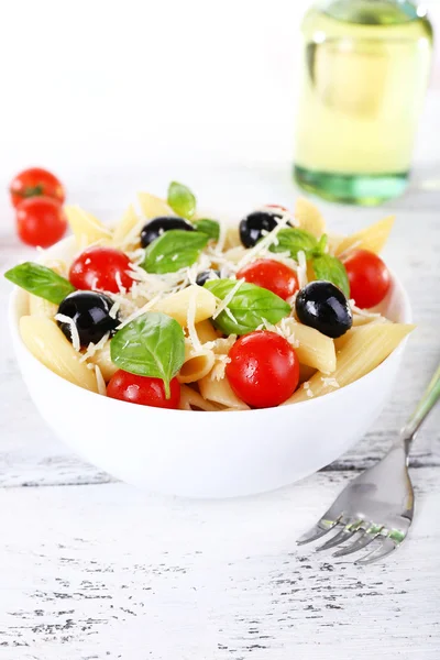 Pasta with tomatoes, olives and basil leaves in bowl on wooden table on natural background — Stock Photo, Image