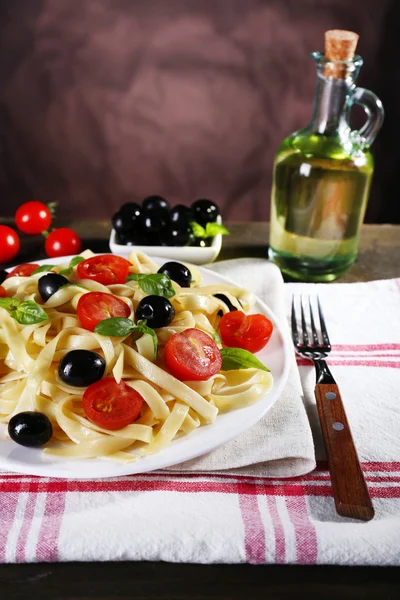 Спагетти с помидорами, оливками и листьями базилика на скатерти на фоне стен — стоковое фото