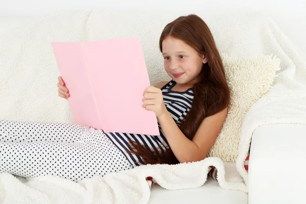 Bella bambina lettura libro sul divano in camera — Foto Stock