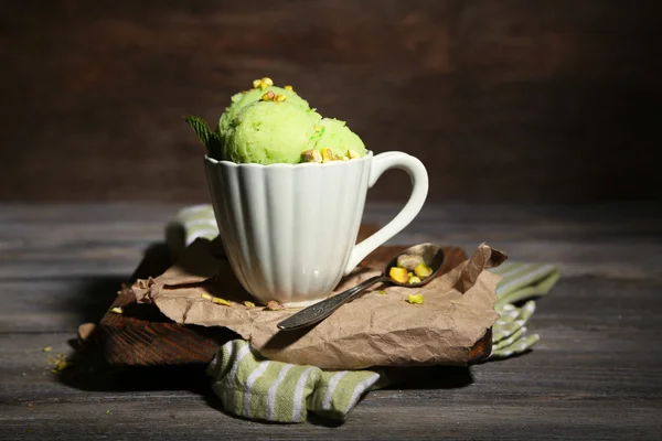 Es krim pistachio lezat dalam cangkir di atas meja kayu, dengan cahaya gelap — Stok Foto
