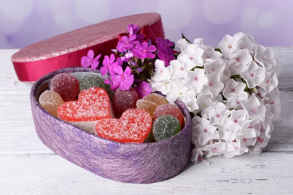 Present box with sweets and flowers on table on bright background — Stock Photo, Image