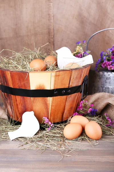 Big round basket with dried grass and fresh eggs on sacking background — Stock Photo, Image