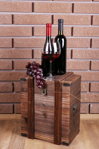 Láhve a sklenice vína a zralých hroznů na box na cihlové zdi pozadí — Stock fotografie