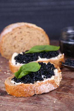 Tereyağı ve ahşap masa üzerinde koyu arka plan üzerinde siyah havyar ile ekmek dilimleri