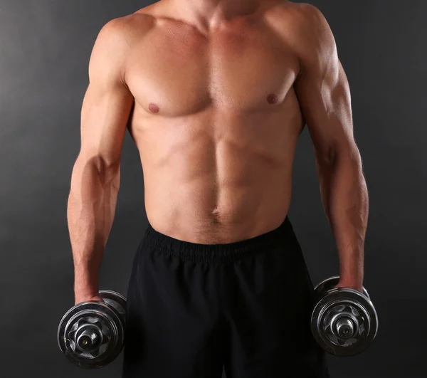 Handsome young muscular sportsman execute exercise with dumbbells on dark background — Stock Photo, Image