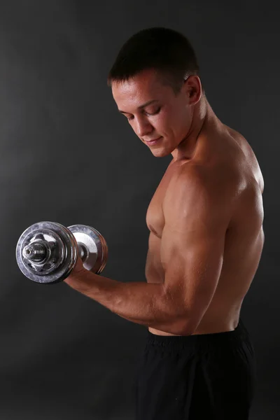 Guapo joven deportista muscular ejecutar ejercicio con mancuerna sobre fondo oscuro —  Fotos de Stock
