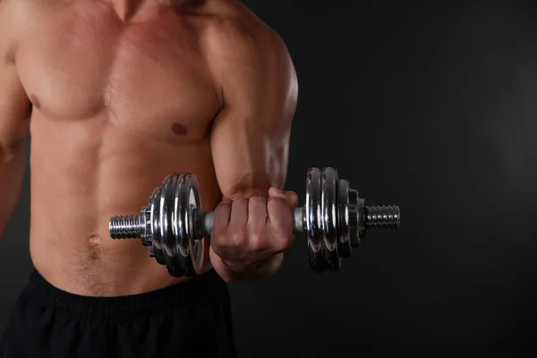 Spier jonge sportman uitvoeren oefening met dumbbell op donkere achtergrond — Stockfoto