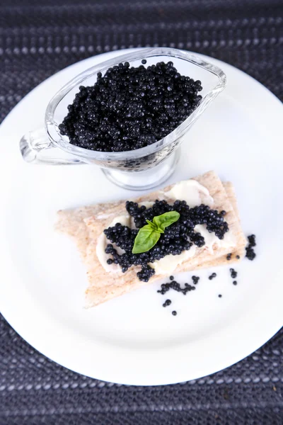 Sneetje brood met boter en sauceboat met kaviaar op plaat op donkere stof achtergrond — Stockfoto