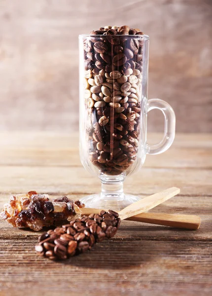 Glass and spoons with coffee beans on wooden table on wooden background — Stock Photo, Image