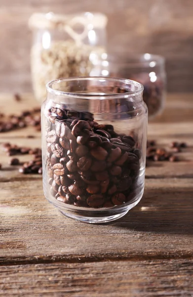 Grains de café dans des bocaux en verre sur table en bois sur fond en bois — Photo