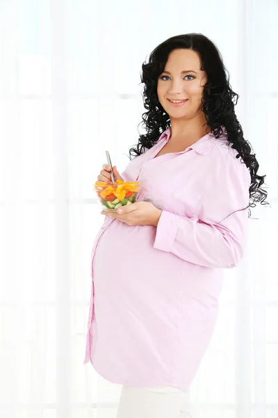 Mujer embarazada joven sosteniendo tazón con ensalada sobre fondo claro —  Fotos de Stock