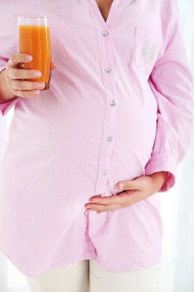 Wanita hamil muda memegang gelas jus dengan latar belakang cahaya — Stok Foto