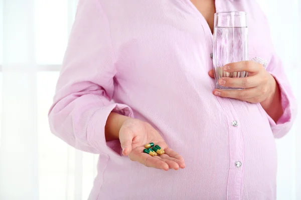 Young pregnant woman holding glass of water and tablets on light background — Stock Photo, Image