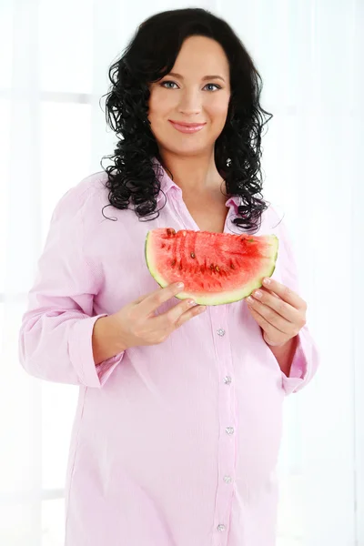 Young pregnant woman holding slice of watermelon on light background — Stock Photo, Image