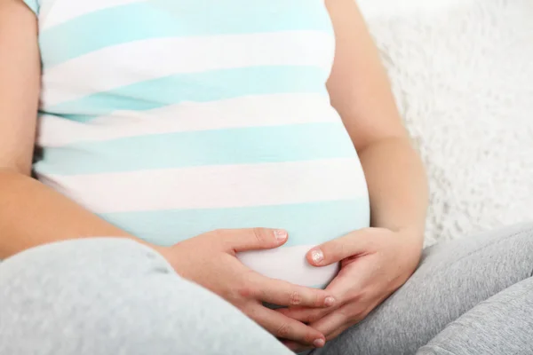 Молодая беременная женщина сидит на диване в комнате — стоковое фото