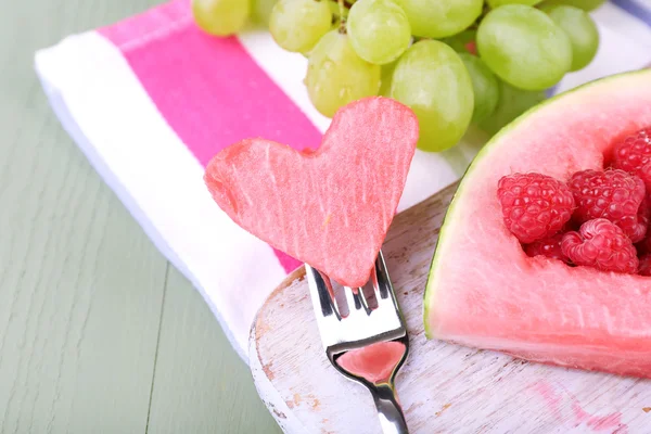 Frische saftige Wassermelonenscheibe mit ausgeschnittener Herzform, gefüllte frische Beeren, auf Schneidebrett, auf Holzgrund — Stockfoto