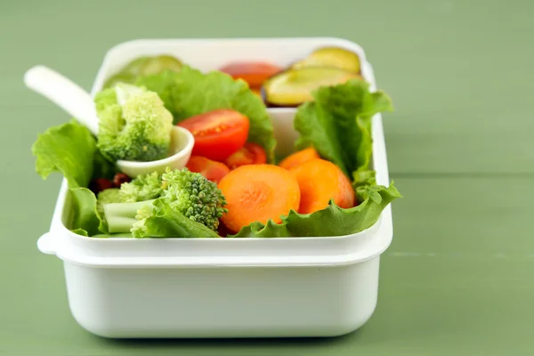 Tasty vegetarian food in plastic box on green wooden table — Stock Photo, Image