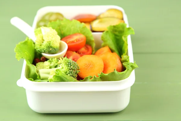 Tasty vegetarian food in plastic box on green wooden table