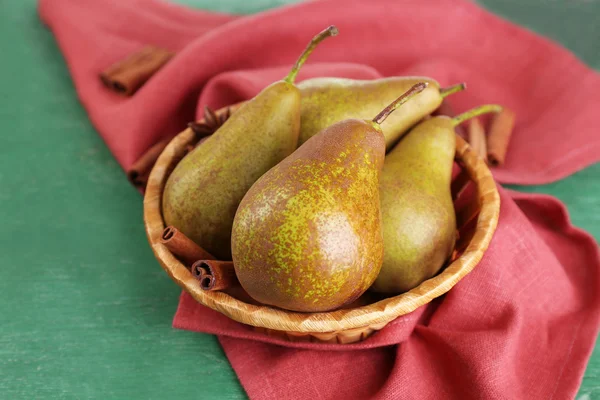 Poires mûres et bâtonnets de cannelle dans un panier en osier, sur fond de bois de couleur — Photo