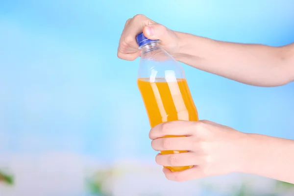 Hand opening bottle with sweet water on sky background — Stock Photo, Image