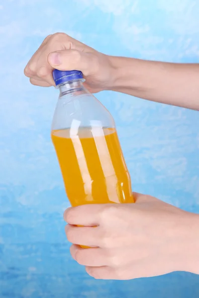 Hand opening bottle with sweet water on blue background — Stock Photo, Image