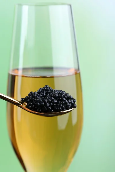 Goblet of champagne and spoon with black caviar on light green background — Stock Photo, Image