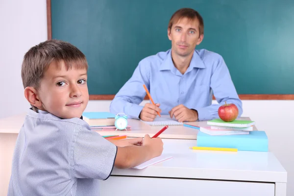 Skolpojke och lärare sitter i klassrummet på blackboard bakgrund — Stockfoto