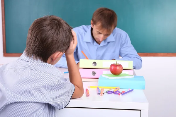 Skolpojke och lärare sitter i klassrummet på blackboard bakgrund — Stockfoto