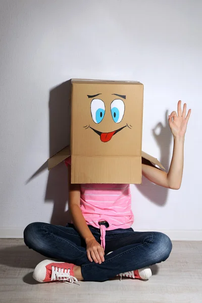 Mujer con caja de cartón en la cabeza con la cara feliz cerca de la pared — Foto de Stock